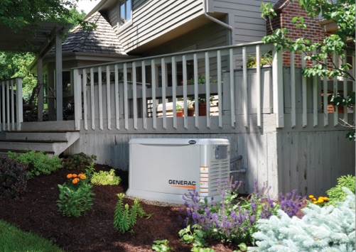 A Generac generator  installed in a garden area outside of a deck attached to a home.